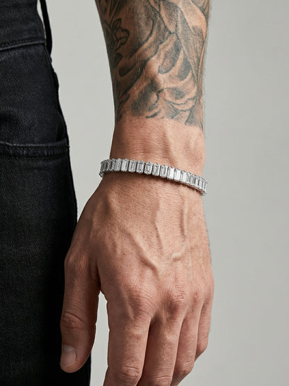 Hand wearing a silver bracelet with a tattooed arm on a neutral background