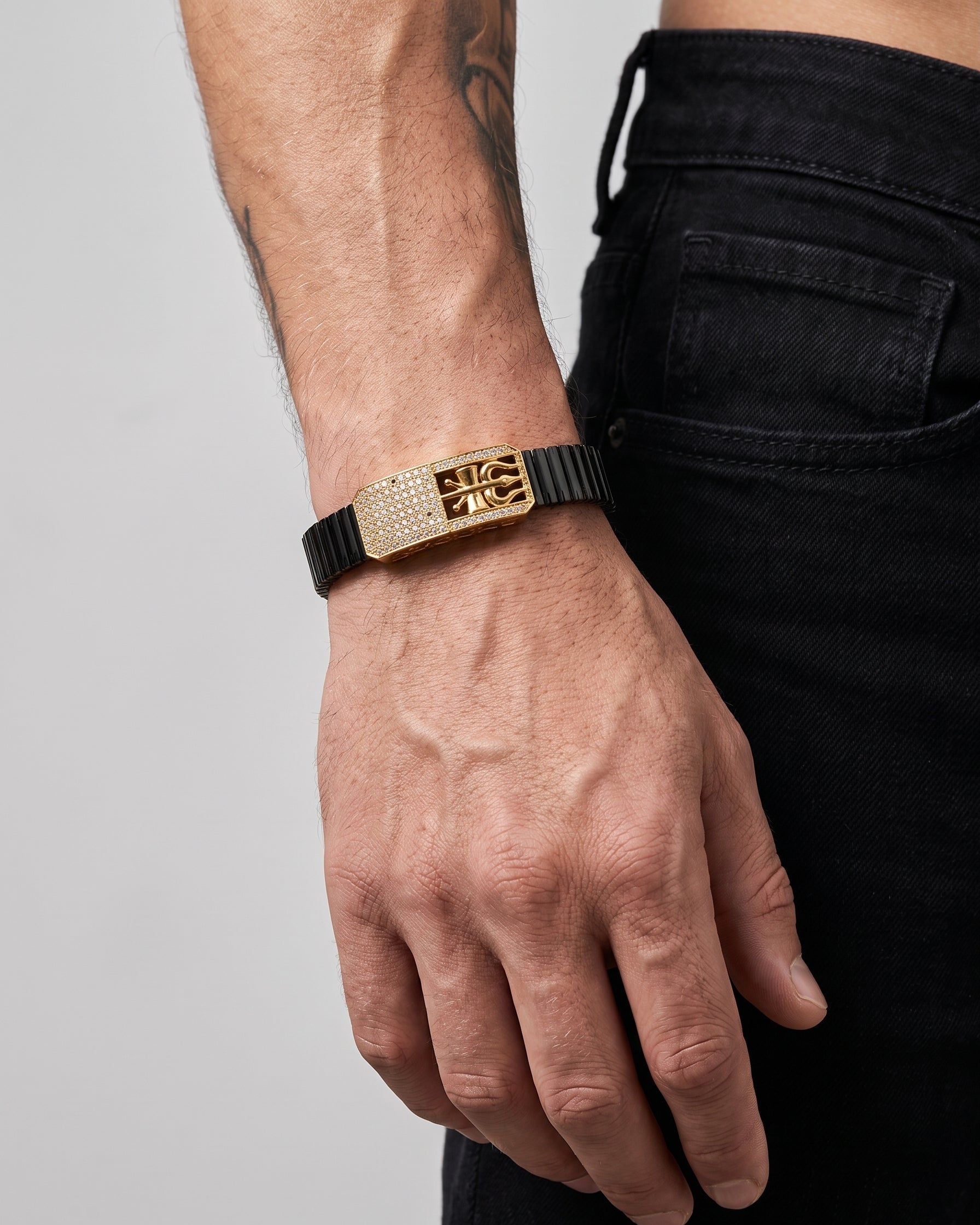 Person wearing a gold bracelet with a black strap on a plain background