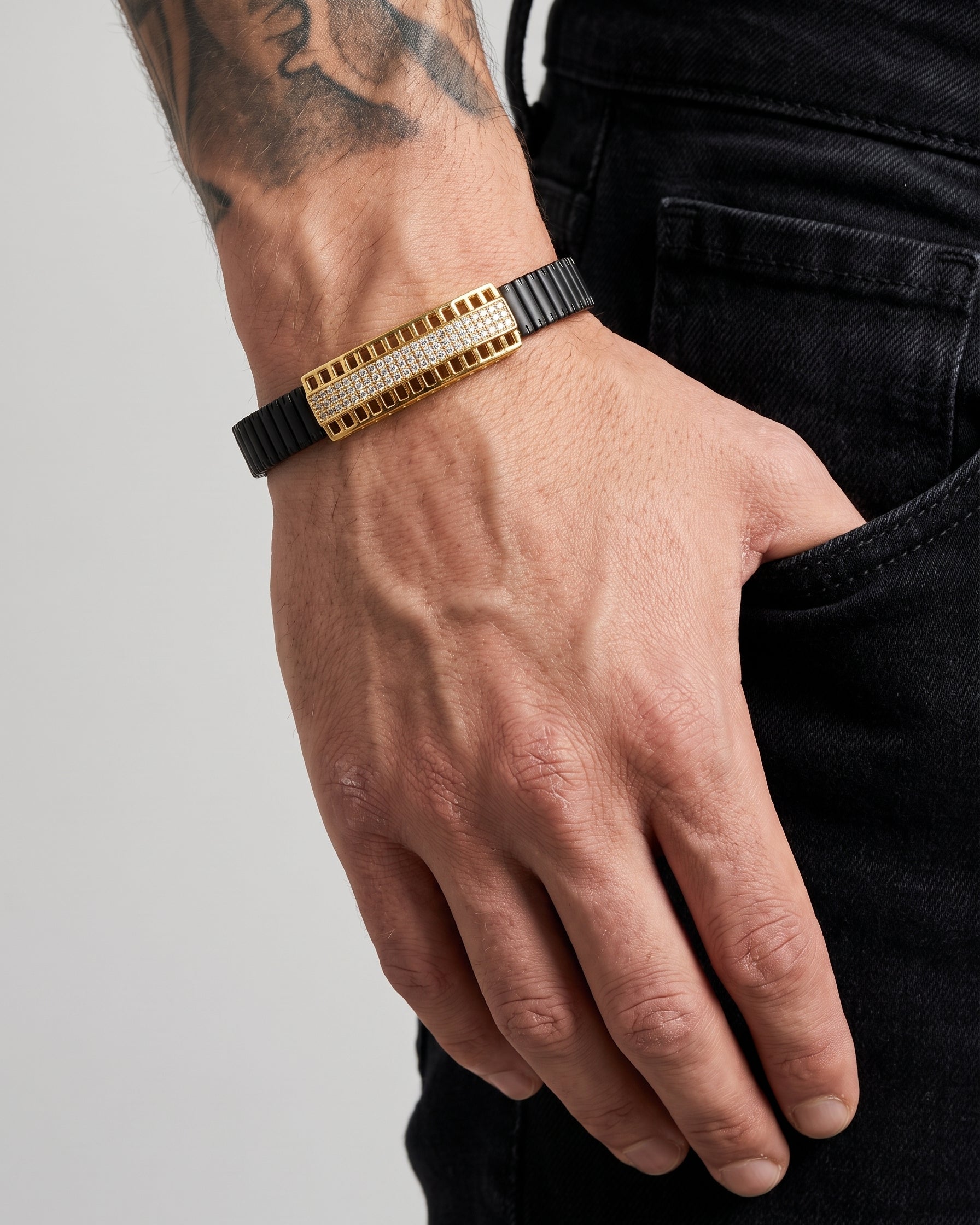 Hand wearing a gold and black bracelet on a plain background