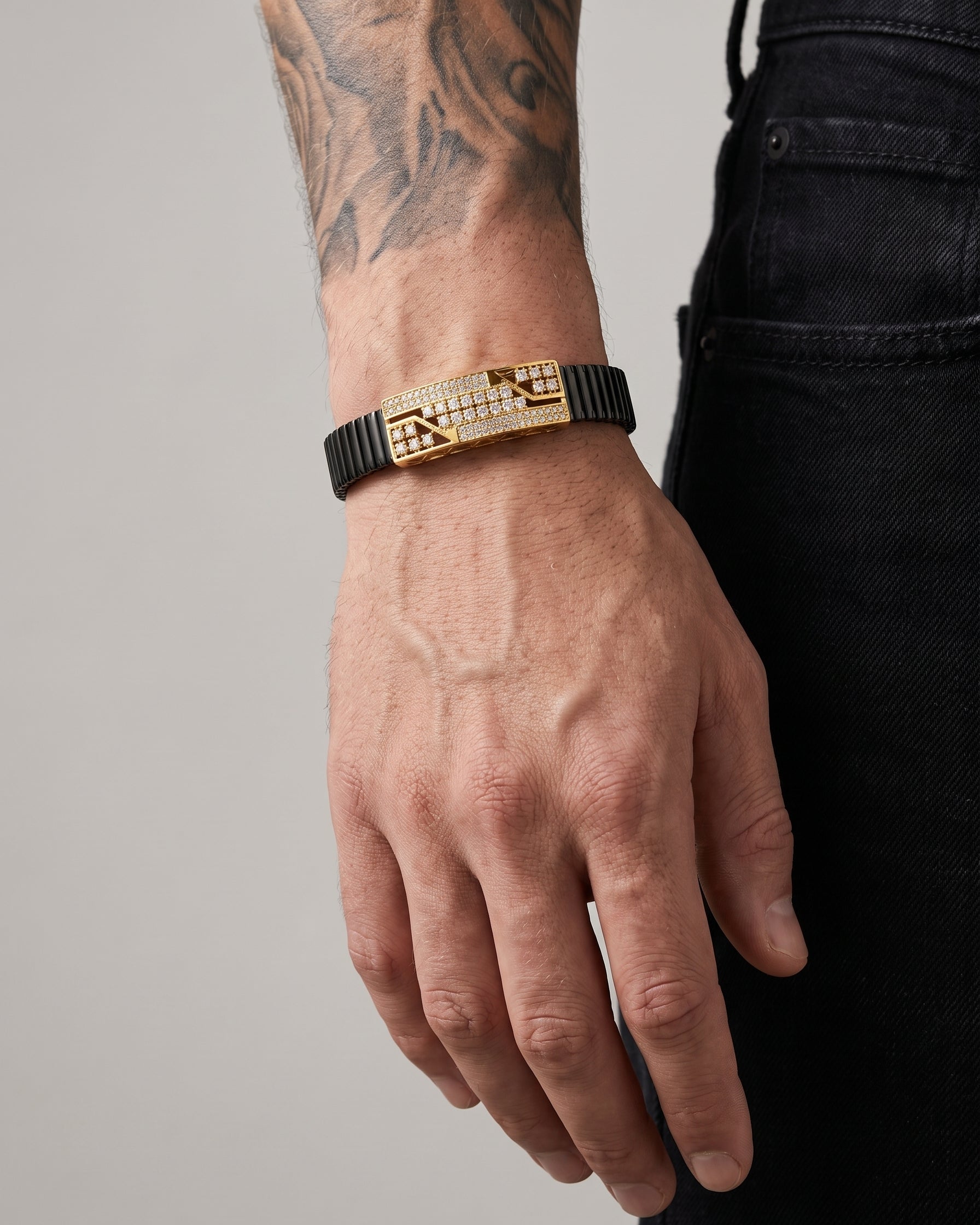 Hand wearing a gold and black bracelet on a neutral background