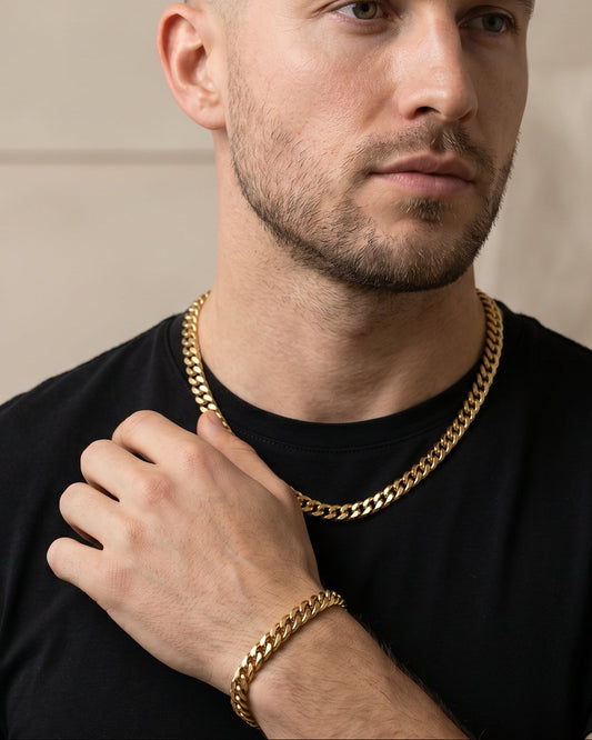 Man wearing a black shirt and gold chain, sitting against a neutral background